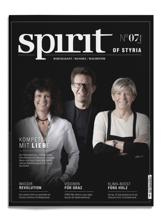 Drei lächelnde Erwachsene - zwei Frauen und ein Mann - stehen gemeinsam auf dem Cover des Magazins "spirit of Styria", Ausgabe 07, vor einem schwarzen Hintergrund.