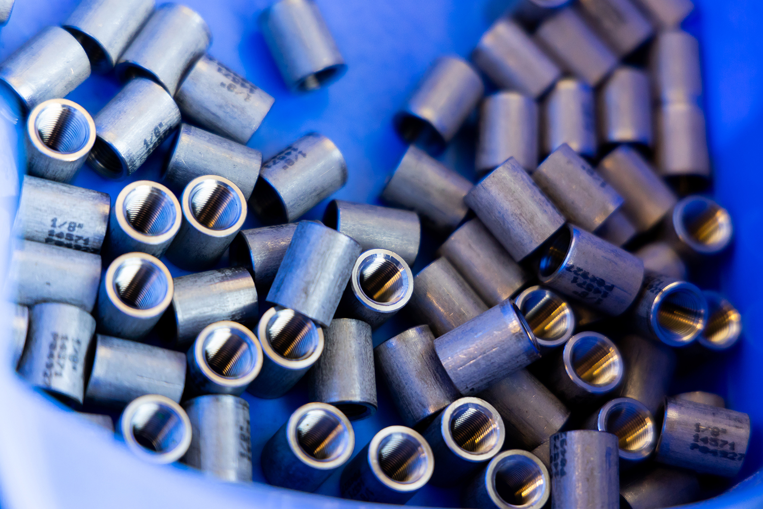 Eine Nahaufnahme zahlreicher zylindrischer Metallhülsen mit hohlem Kern, die in einem blauen Behälter verstreut sind.