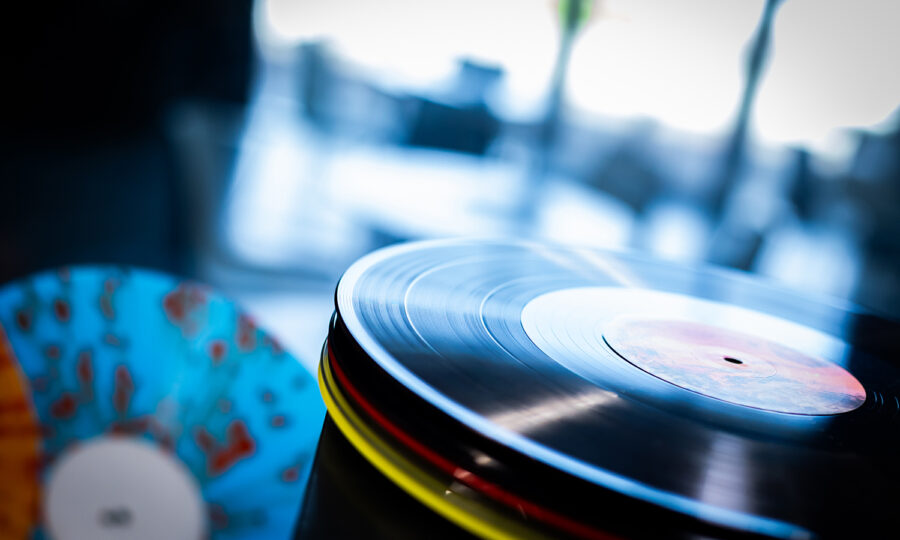 Nahaufnahme von zwei Schallplatten, einer schwarzen mit rotem Etikett in der Mitte auf einem Plattenteller und einer anderen mit einem blau-orange marmorierten Muster, mit unscharfem Hintergrund.