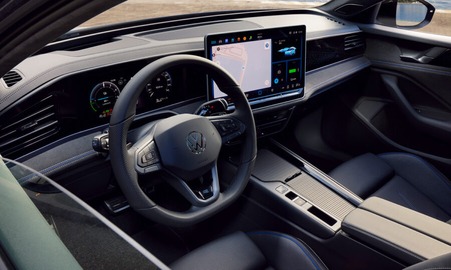 Das Bild zeigt den Innenraum eines Volkswagen mit einem modernen Cockpit mit digitalem Kombiinstrument, einem großen zentralen Touchscreen für die Navigation und einem lederbezogenen Lenkrad mit Bedientasten.