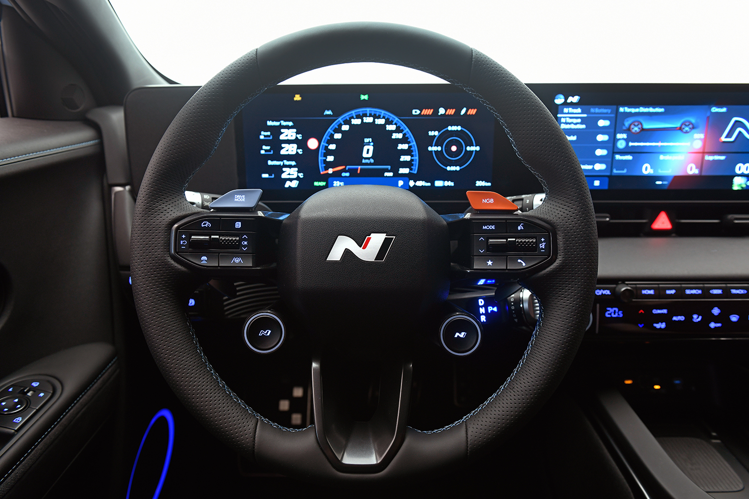 Nahaufnahme eines Autolenkrads mit dem "N"-Performance-Logo, mit beleuchteten Bedientasten und einer digitalen Anzeige im Armaturenbrett mit Tachometer, Navigation und verschiedenen Fahrzeuginformationen.