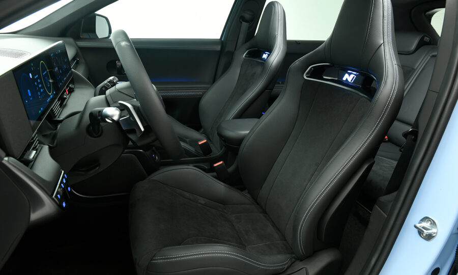 Der Innenraum eines modernen Autos mit sportlichen schwarzen Vordersitzen mit "N"-Logo, einem digitalen Armaturenbrett, einem Lenkrad und schlanken, minimalistischen Bedienelementen. Der Innenraum hat ein hochtechnologisches, leistungsorientiertes Design.