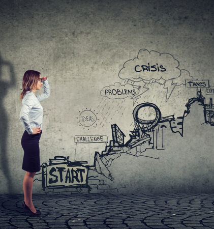 Eine Frau in Geschäftskleidung steht selbstbewusst da und blickt auf eine Wandillustration, die einen Weg vom "Start" zum "Ziel" zeigt, mit Hindernissen wie "Probleme", "Krise" und "Wettbewerb". Ihr Schatten erscheint in Form eines Superhelden.