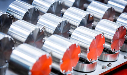 Reihen glänzender, zylindrischer Metallteile mit Schraubendetails sind sauber auf einer Metalloberfläche angeordnet und reflektieren das Licht mit einem polierten, industriellen Aussehen.