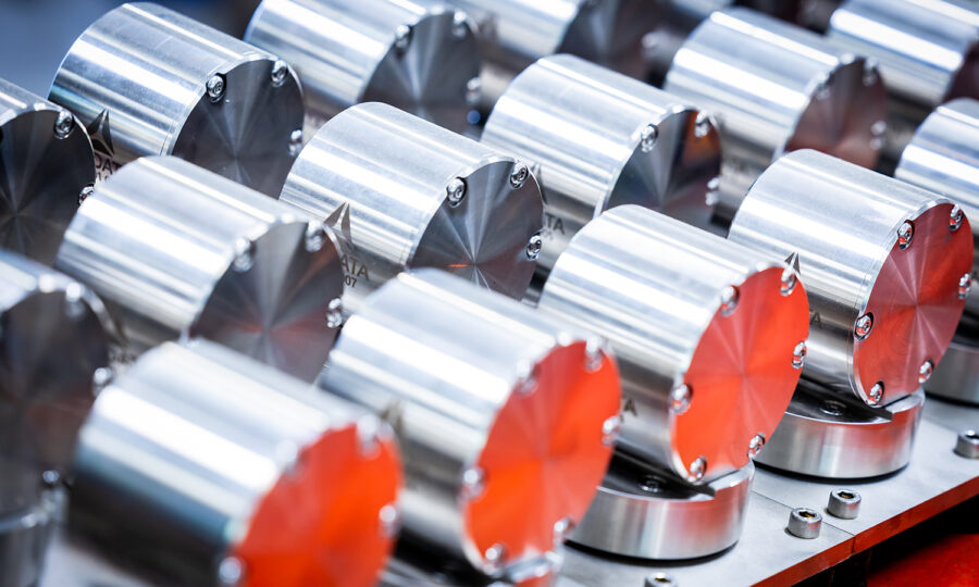 Reihen glänzender, zylindrischer Metallteile mit Schraubendetails sind sauber auf einer Metalloberfläche angeordnet und reflektieren das Licht mit einem polierten, industriellen Aussehen.