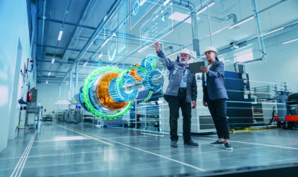 Zwei Ingenieure mit Schutzhelmen stehen in einer modernen Industrieanlage und interagieren mit einer großen, transparenten digitalen Projektion mechanischer Maschinenteile, um das Design zu diskutieren oder zu analysieren.