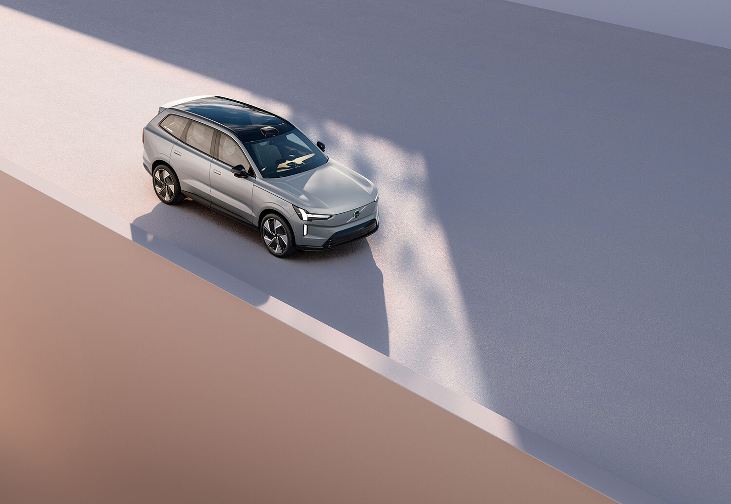 Ein silberner Geländewagen mit schwarzem Dach ist auf einer flachen, offenen Fläche geparkt, die von den umliegenden Wänden mit weichen Schatten versehen ist, was eine minimalistische und moderne Atmosphäre schafft.