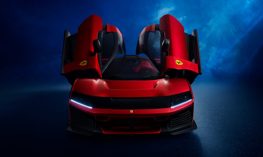 Ein roter Ferrari-Sportwagen mit geöffneten Flügeltüren wird von vorne vor einem dunklen, blau beleuchteten Hintergrund gezeigt. Die Scheinwerfer sind eingeschaltet, und auf den Türen sind die Ferrari-Logos zu sehen.