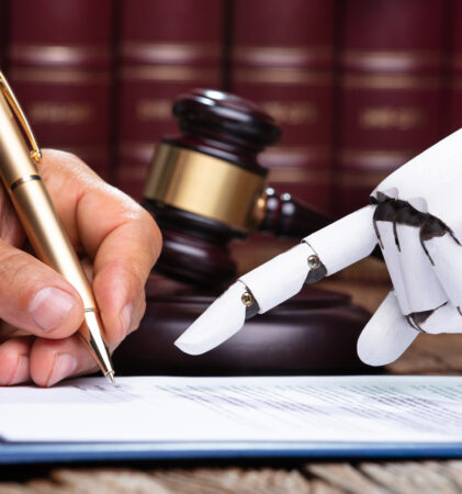 Eine menschliche Hand unterschreibt ein juristisches Dokument mit einem Stift, während eine Roboterhand auf das Papier zeigt; im Hintergrund sind der Hammer eines Richters und Gesetzesbücher zu sehen.