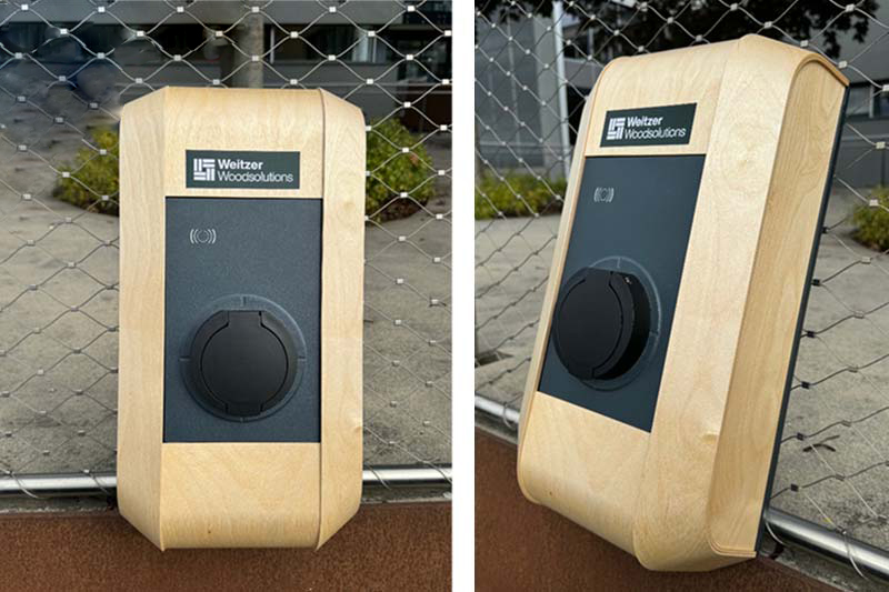 Zwei Ansichten einer rechteckigen Ladestation für den Außenbereich mit einem hellen Holzrahmen und einer schwarzen Frontplatte, die an einem Zaun montiert ist. Die Platte zeigt das Logo "Weitzer Woodsolutions" und einen runden Ladeanschluss.