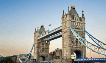 Die Tower Bridge in London mit ihren zwei Türmen und blauen Hängebrücken überspannt die Themse bei Sonnenuntergang. Der Himmel ist klar, und das Wort "Spirit" erscheint in der unteren rechten Ecke.