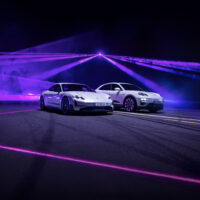 Zwei schnittige, weiße Sportwagen parken nebeneinander auf einer dunklen Straße, beleuchtet von dramatischen lila und rosa Neonlichtern und Laserstrahlen im Hintergrund.