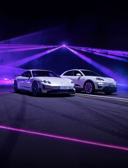 Zwei schnittige, weiße Sportwagen parken nebeneinander auf einer dunklen Straße, beleuchtet von dramatischen lila und rosa Neonlichtern und Laserstrahlen im Hintergrund.
