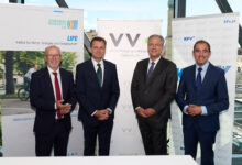 Vier Männer in Business-Kleidung stehen lächelnd vor Bannern von Joanneum Research LIFE, Versicherungsverband Österreich, KFV.at und der langen Tafel Graz in einem modernen Glasgebäude mit Stadtblick.