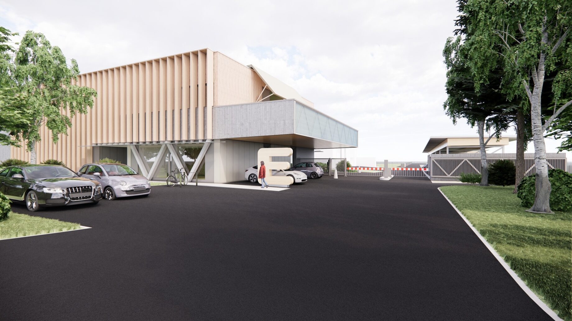 Modernes Gebäude mit Holz- und Betonfassade, großen Fenstern und überdachtem Eingang nahe der langen Tafel Graz. Mehrere geparkte Autos und eine Person, die in der Nähe spazieren geht. In der Umgebung gibt es grünes Gras, Bäume und einen klaren Himmel.