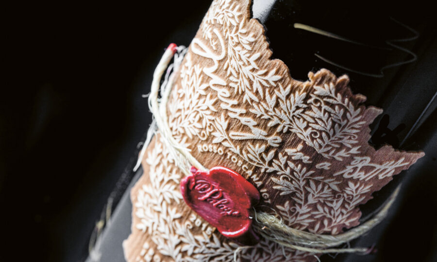 Nahaufnahme einer Weinflasche mit einem verschnörkelten, blattgemusterten Etikett, das mit einer Schnur gebunden und mit einem roten Wachsstempel versiegelt ist. Der Hintergrund ist dunkel und hebt das komplizierte Design der Flasche hervor.