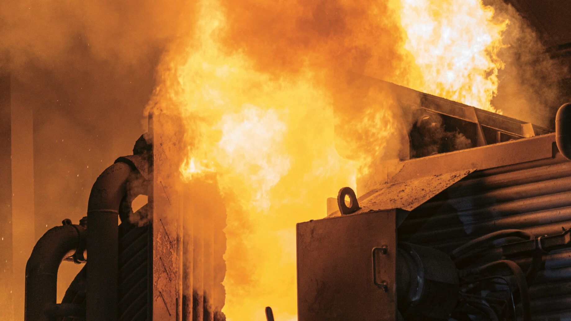 Große Flammen und dichter Rauch verschlingen Industriemaschinen in einer Fabrik und schaffen eine intensive und gefährliche Szene. Das Bild fängt die Hitze und die Gefahr eines Brandes in einer industriellen Umgebung ein.