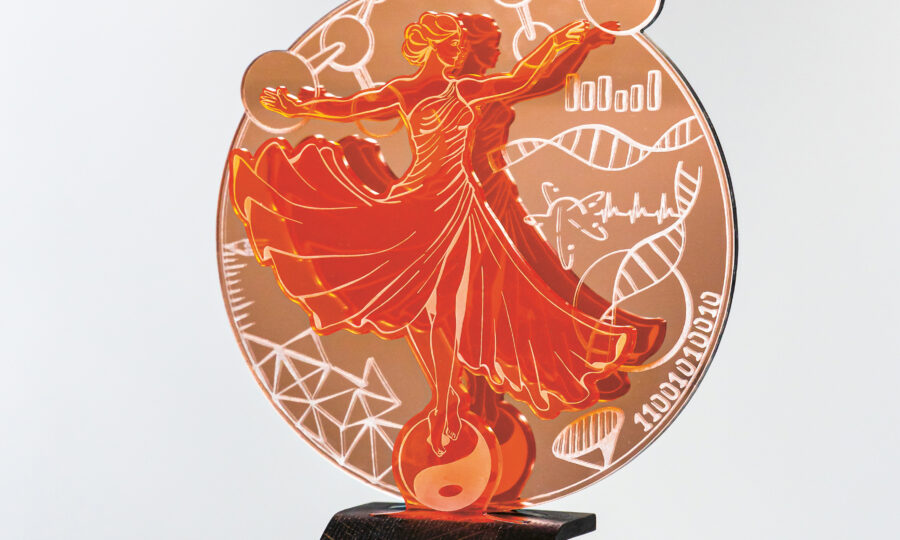 Ein orangefarbener Acryl-Award mit einer stilisierten tanzenden Frau, umgeben von wissenschaftlichen Symbolen wie DNA-Strängen, Molekülen und geometrischen Formen, montiert auf einem schwarzen Ständer.