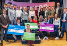 Eine Gruppe von Personen posiert in einem Innenraum bei einer Veranstaltung der Ortskernbelebung Steiermark. Drei von ihnen halten große Preisschecks über 2.000 €, 1.500 € und 1.000 € in der Hand. Vorne sitzt eine Frau mit einem 500-Euro-Scheck. Alle lächeln.