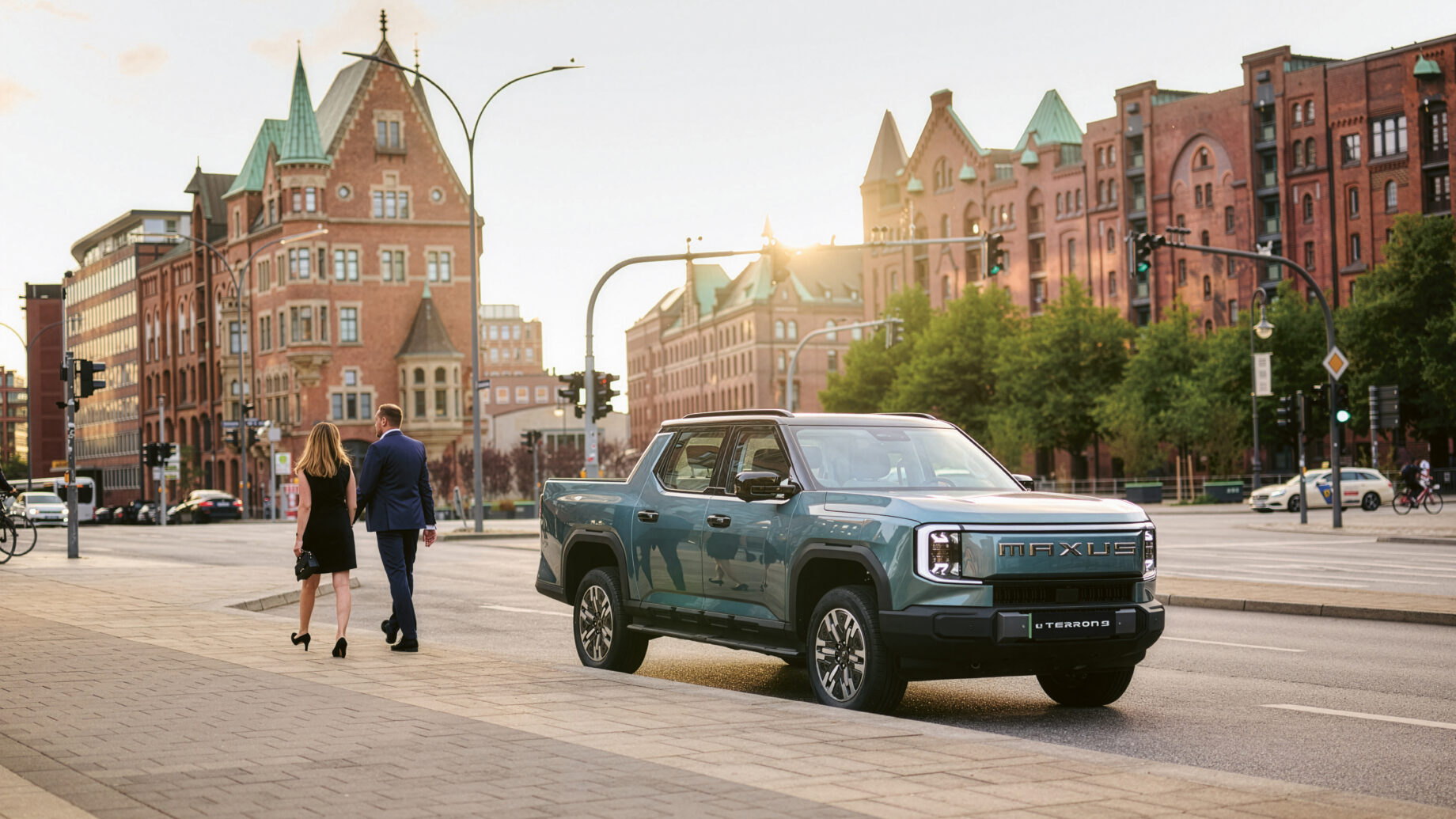 Ein grüner Maxus T90 EV Pickup parkt auf einer Stadtstraße, während ein Paar in der Nähe spazieren geht, mit historischen Backsteingebäuden im Hintergrund.