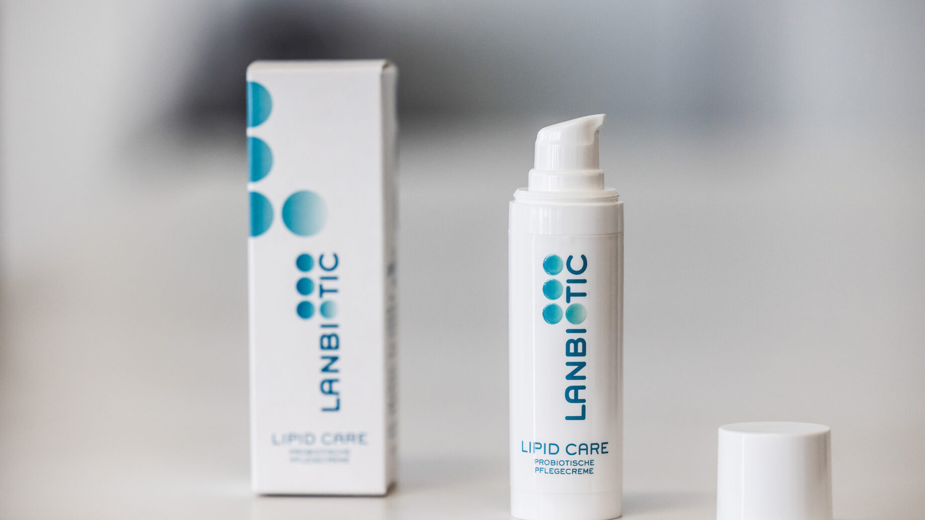 Eine weiße Lanbiotic Lipid Care Hautpflegeflasche mit einer Pumpe, deren Verschluss entfernt wurde, steht neben ihrer Verpackung auf einer weißen Fläche.