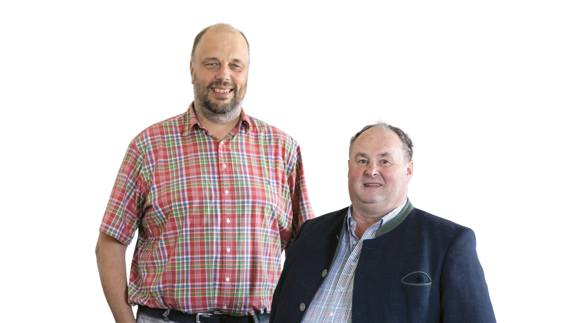 Zwei nebeneinander stehende Männer mittleren Alters, der eine größer in einem kurzärmeligen karierten Hemd und einer hellen Hose, der andere kleiner in einem dunklen Blazer über einem karierten Hemd. Beide lächeln vor einem weißen Hintergrund.
