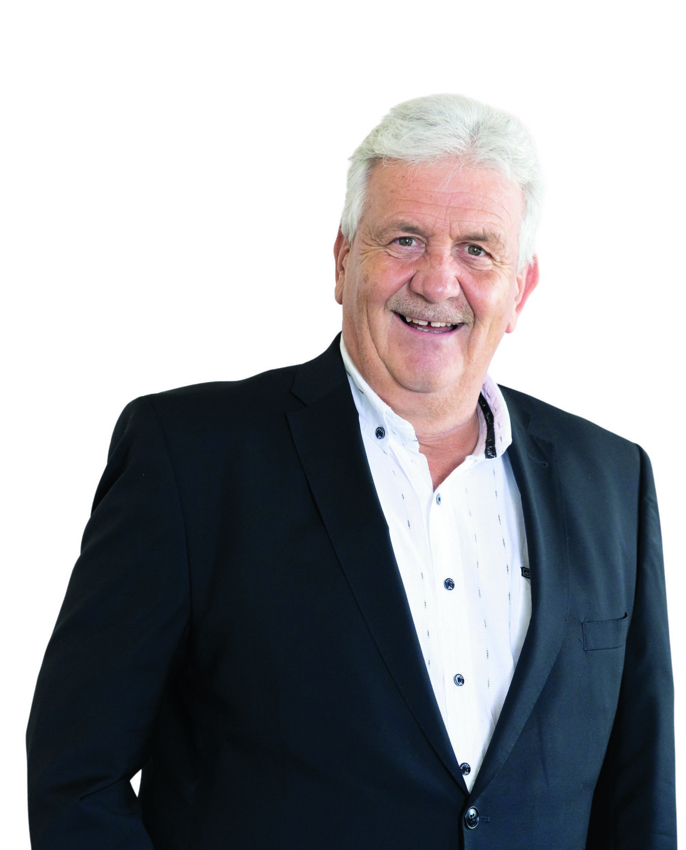 Älterer Mann mit weißem Haar in einem schwarzen Blazer und weißem Hemd, lächelnd, vor einem schlichten weißen Hintergrund.