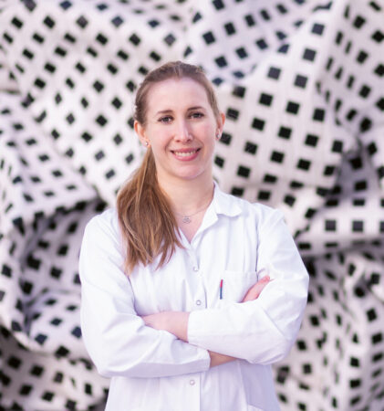 Zwei Personen, eine in einem Laborkittel und eine in einer Weste, stehen vor einer großen, zerknitterten, schwarz-weiß-karierten Stoffinstallation.