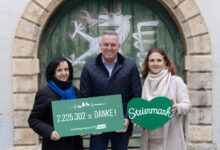 Drei Personen lächeln vor einer bemalten Pferdetür, die "2.225.302 x DANKE!" und ein grünes Herz mit "Steiermark"-Batterie-Innovationstagen in Graz hält.