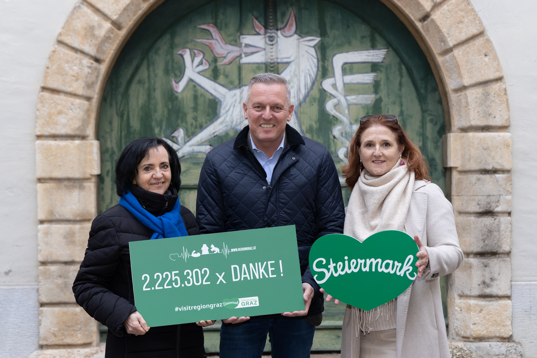 Drei Personen lächeln vor einer bemalten Pferdetür, die "2.225.302 x DANKE!" und ein grünes Herz mit "Steiermark"-Batterie-Innovationstagen in Graz hält.