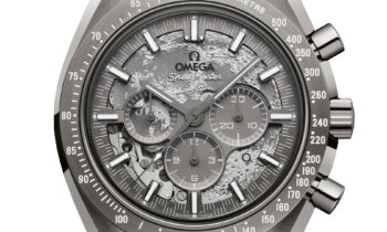 Eine silberne Omega Speedmaster Uhr mit einem strukturierten grauen Zifferblatt, drei Hilfszifferblättern, einer Tachymeter-Lünette und einem schwarzen Stoffarmband.