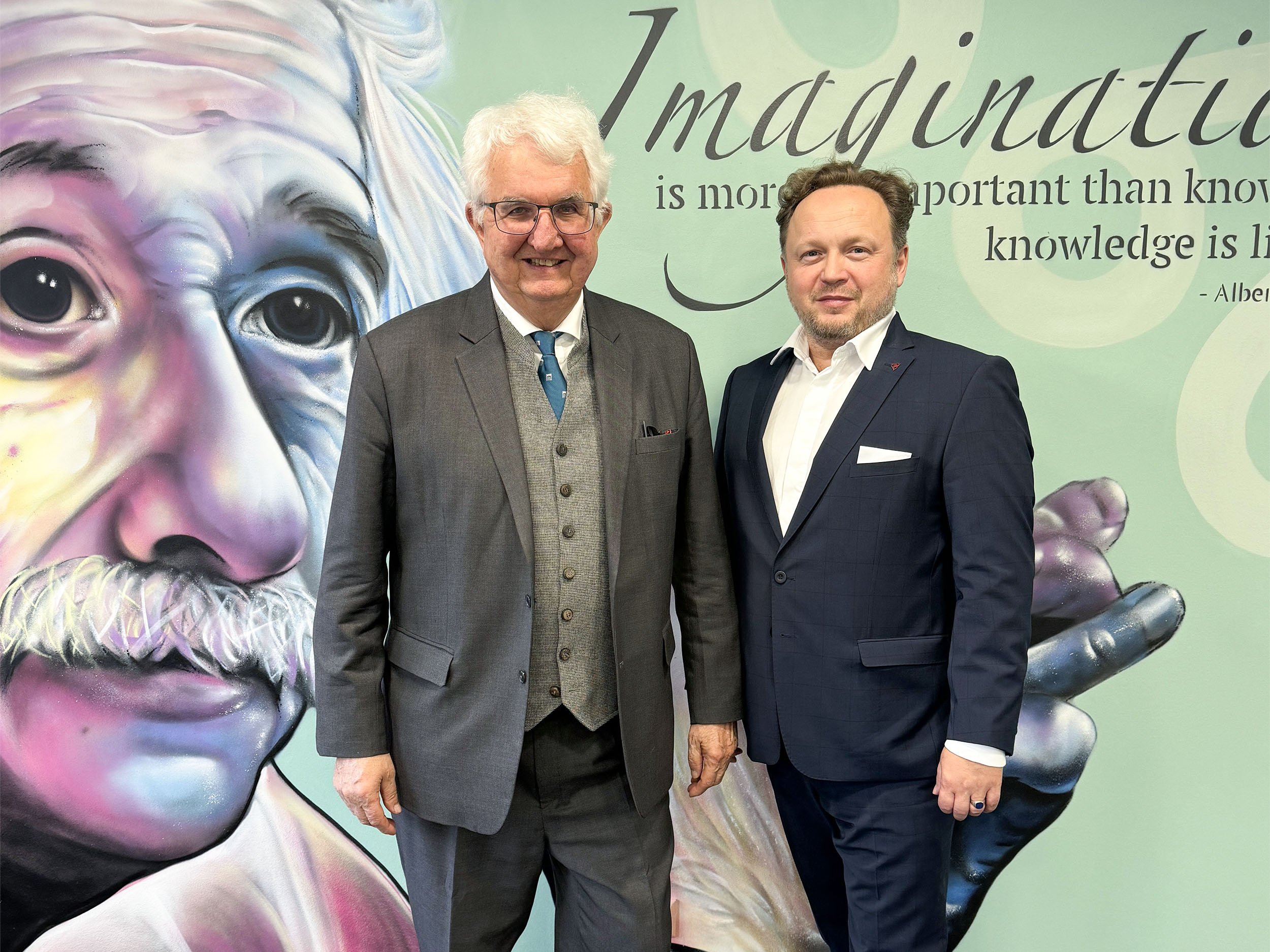 Zwei Männer in Anzügen stehen vor einem Wandbild von Einstein, als die Energie Steiermark startet Bau Logistikzentrum in Frohnleiten mit Phantasie und Wissen inspiriert.