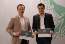 Zwei Männer in Blazern lächeln mit Urkunden bei den Battery Innovation Days in Graz: Den Standort Steiermark neu aufladen, Wappen und grüner Löwe im Hintergrund.