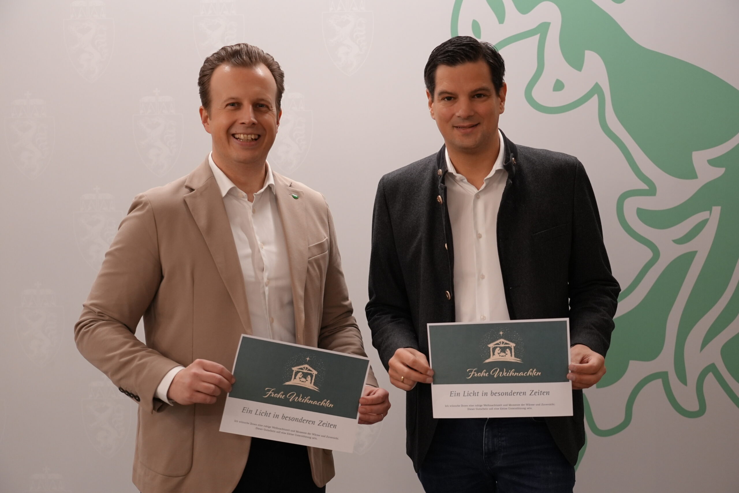 Zwei Männer in Blazern lächeln mit Urkunden bei den Battery Innovation Days in Graz: Den Standort Steiermark neu aufladen, Wappen und grüner Löwe im Hintergrund.