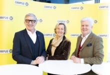 Drei lächelnde Erwachsene in Business-Kleidung posieren vor einem leuchtend gelben "CAMPUS 02"-Hintergrund, um 75 Jahre Bauernbundball in der Steiermark zu feiern.