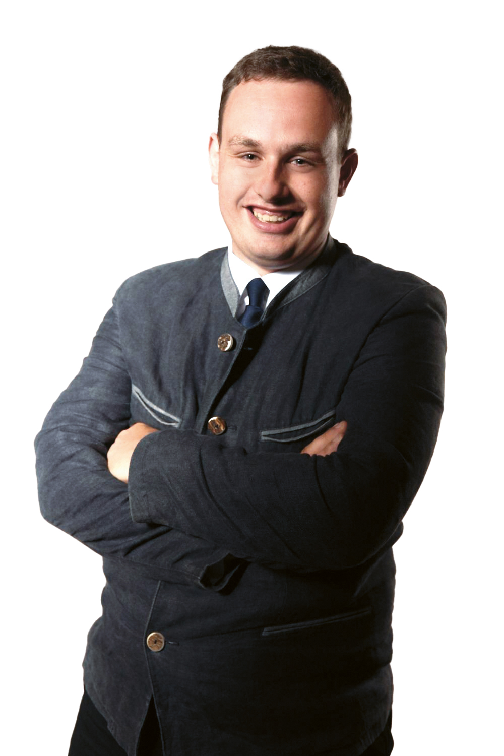 Mann in dunkler Jacke und Krawatte, lächelnd mit verschränkten Armen, stehend vor weißem Hintergrund.