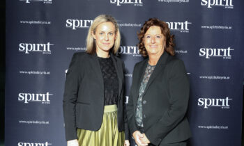 Zwei Frauen stehen lächelnd vor einem "spirit of styria" Step-and-Repeat-Hintergrund bei einer Veranstaltung.