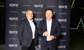 Zwei Männer in Anzügen stehen bei einer Veranstaltung lächelnd vor einem schwarzen "Spirit of Styria" Step-and-Repeat-Banner.