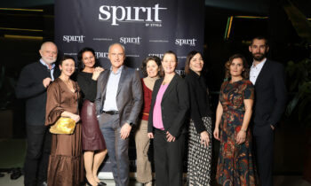 Eine Gruppe von Menschen posiert lächelnd vor einer schwarzen "Spirit of Styria"-Kulisse bei einer Indoor-Veranstaltung.