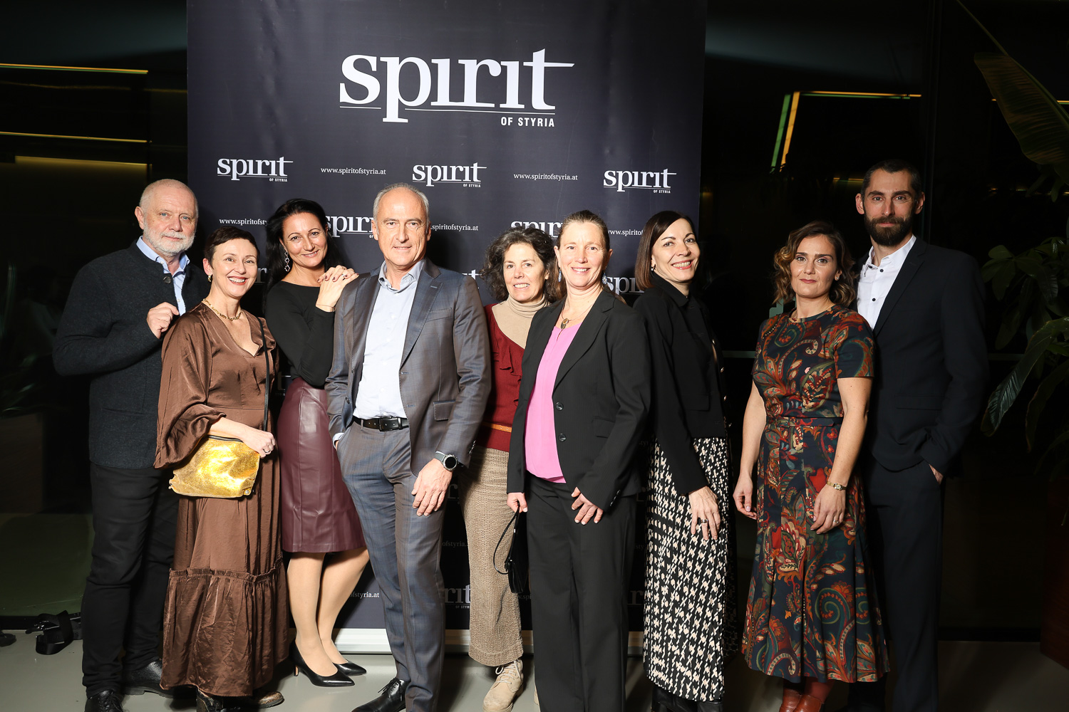 Eine Gruppe von Menschen posiert lächelnd vor einer schwarzen "Spirit of Styria"-Kulisse bei einer Indoor-Veranstaltung.
