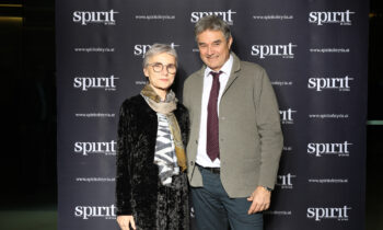 Eine Frau und ein Mann stehen bei einer Veranstaltung lächelnd vor einem schwarzen "Spirit of Styria"-Werbebanner.