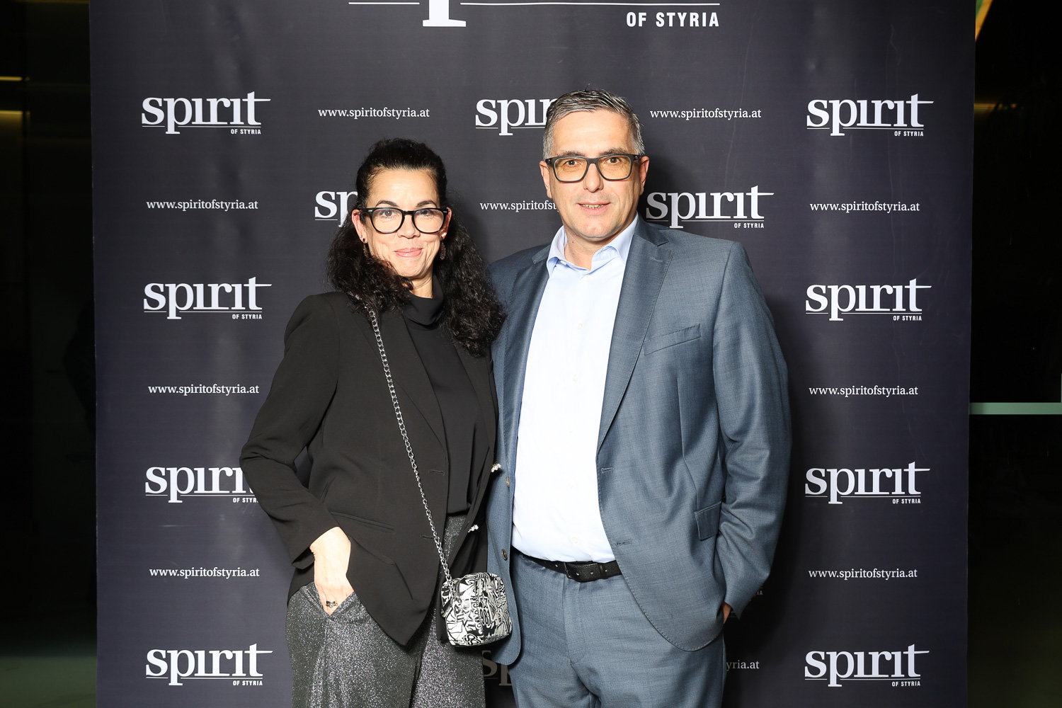 Eine Frau und ein Mann posieren gemeinsam lächelnd vor einer Step-and-Repeat-Kulisse mit dem "Spirit of Styria"-Logo.
