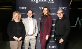 Vier Personen stehen lächelnd vor einem "spirit of styria"-Hintergrund bei einer Veranstaltung, gekleidet in Business- und Smart-Casual-Kleidung.