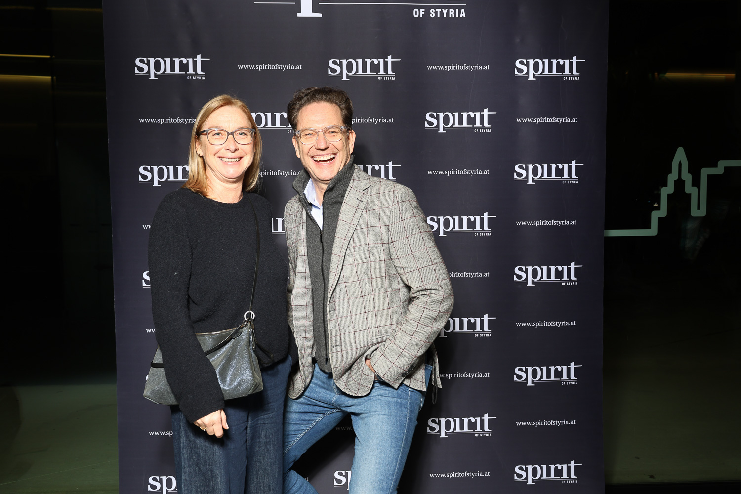 Zwei Personen lächeln und posieren gemeinsam vor einem schwarzen Step-and-Repeat-Hintergrund mit "spirit of Styria"-Logos.