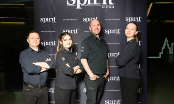 Vier Personen in schwarzen Uniformen stehen lächelnd vor einer Kulisse mit dem Schriftzug "Spirit of Styria" in einem gut beleuchteten Innenbereich.