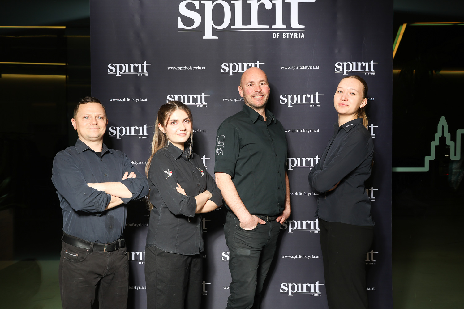 Vier Personen in schwarzen Uniformen stehen lächelnd vor einer Kulisse mit dem Schriftzug "Spirit of Styria" in einem gut beleuchteten Innenbereich.