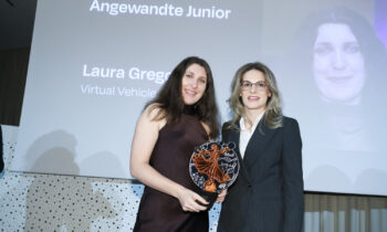Zwei Frauen stehen lächelnd bei einer Preisverleihung. Eine von ihnen hält eine dekorative Trophäe; auf dem Bildschirm hinter ihnen steht "2. Platz Angewandte Junior Laura Gregorich".