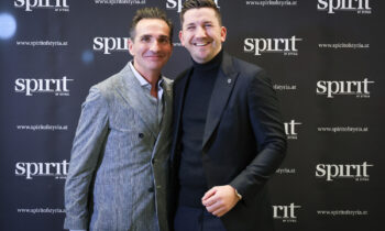 Zwei Männer in formeller Kleidung lächeln und posieren zusammen vor einem schwarzen "Spirit of Styria"-Schritt- und Wiederholungskulisse.
