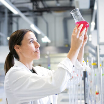 Ein Wissenschaftler in einem weißen Laborkittel untersucht einen Kolben mit einer rosafarbenen Flüssigkeit in einem modernen Labor.