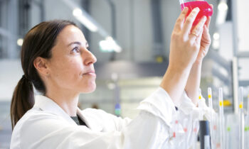 Ein Wissenschaftler in einem weißen Laborkittel untersucht einen Kolben mit einer rosafarbenen Flüssigkeit in einem modernen Labor.